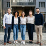 A real photograph of a confident small business team standing together outside their workplace or office entrance, conveying authenticity, approachability, and trust.
